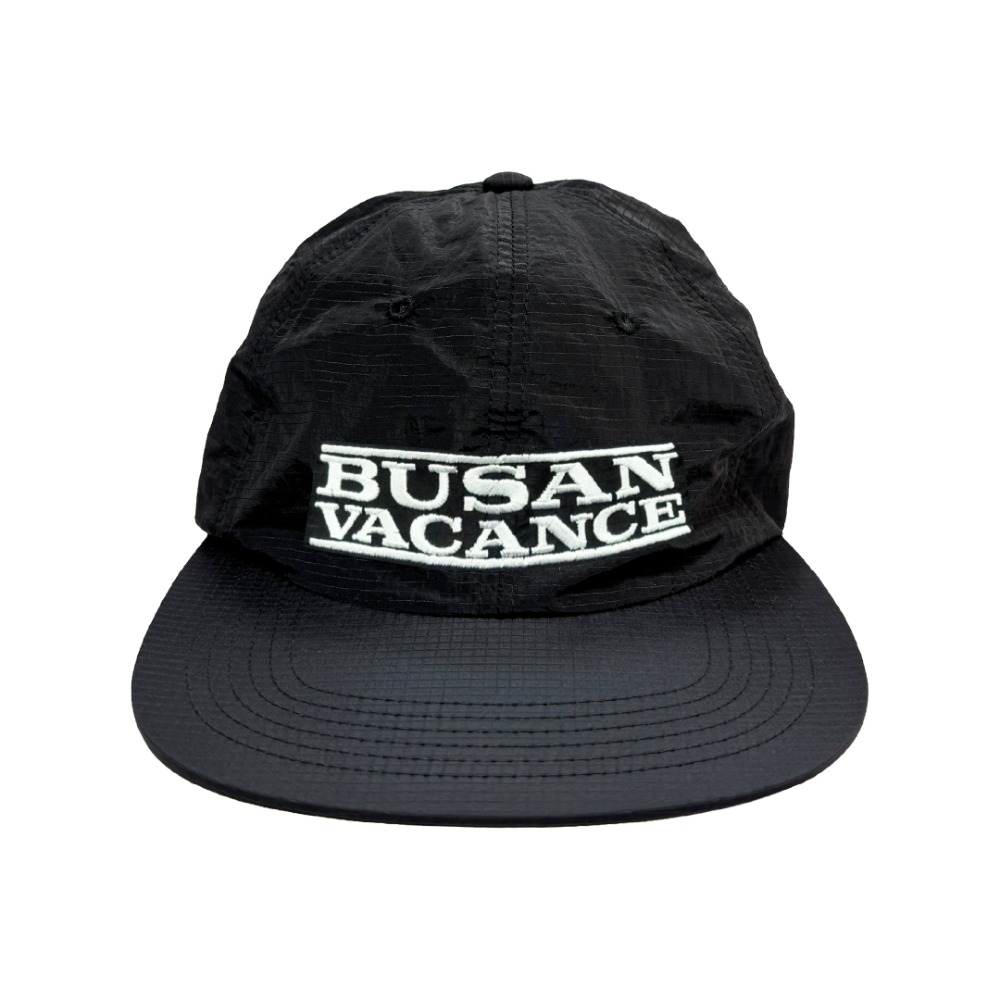 블랙 립스탑 나일론 캡. 앞면에 화이트 아웃라인 박스 안 'BUSAN VACANCE' 화이트 자수, 챙은 거의 평평한 형태