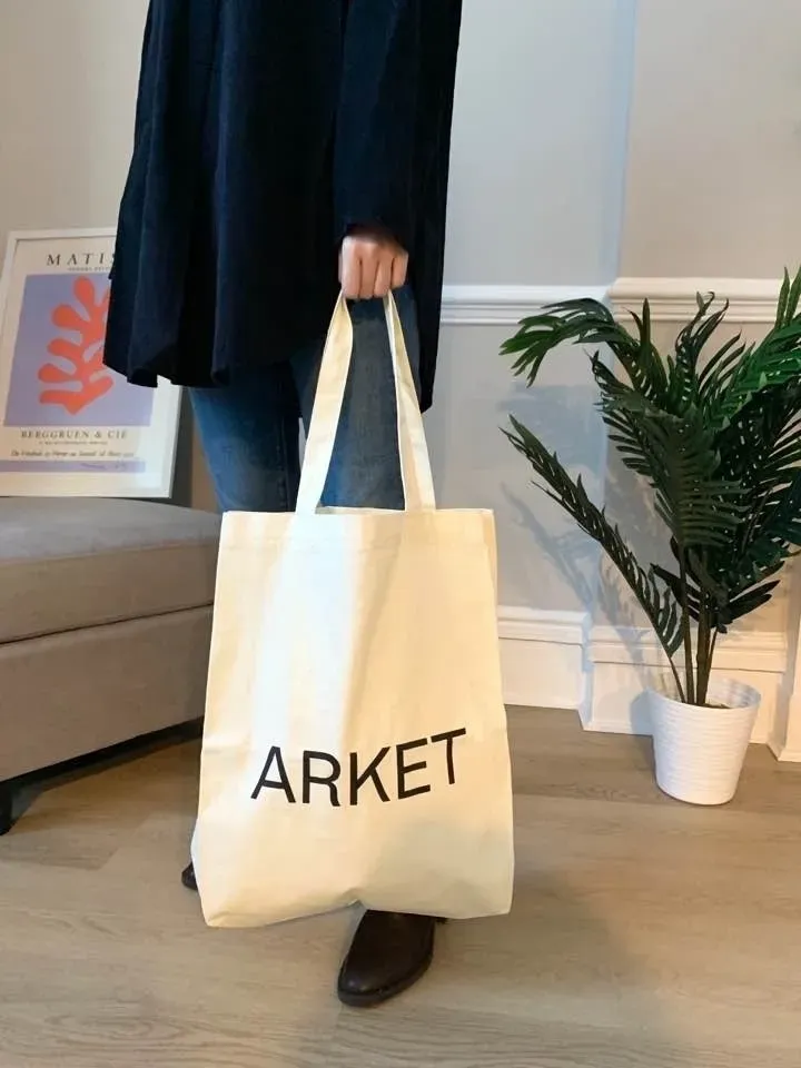 아이보리 캔버스 토트백. 앞면 중앙에 블랙 'ARKET' 대형 레터링이 있다