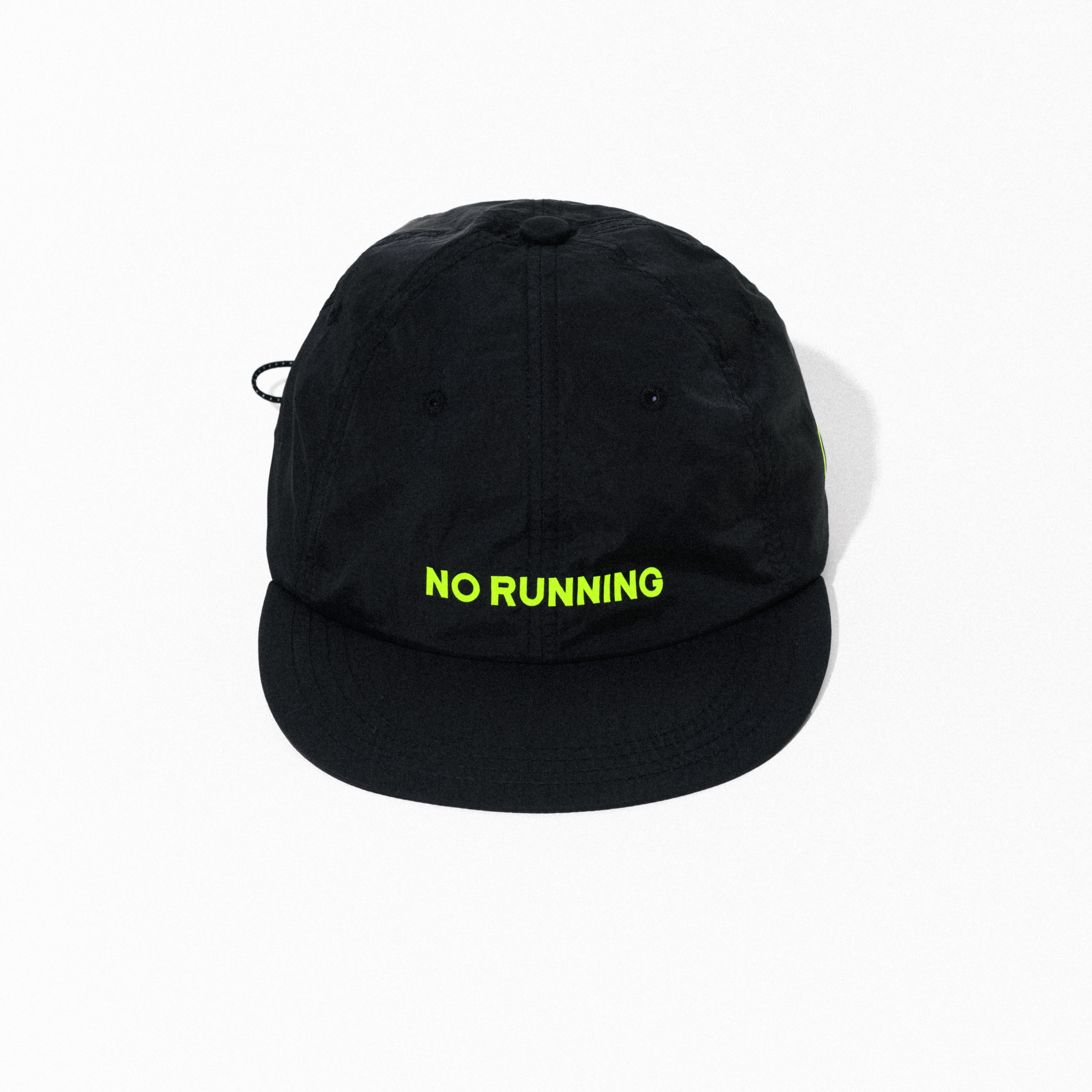 블랙 나일론 6패널 캡. 앞면 아래쪽 중앙에 네온 옐로 'NO RUNNING' 레터링 프린트, 짧고 평평한 챙과 측면 스트링 고리