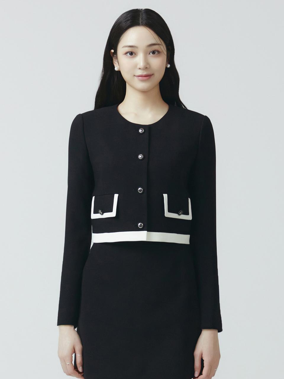칼라 없는 라운드넥에 앞 중앙 일렬 4개 버튼(블랙 바탕에 은색 테두리) 여밈. 가슴 아래 좌우 대칭으로 플랩 패치 포켓 2개가 달렸고 플랩 가장자리에 아이보리 배색 트림이 둘러져 있으며 각 플랩마다 작은 버튼 1개가 붙어 있다. 밑단에는 같은 아이보리 색 가로 배색 밴드가 한 줄 들어간다. 허리선 위에서 끝나는 크롭 기장에 소매는 긴소매이고 립·시보리 없이 평평하게 마감됐다. 무지 블랙 원단으로 패턴은 없다.