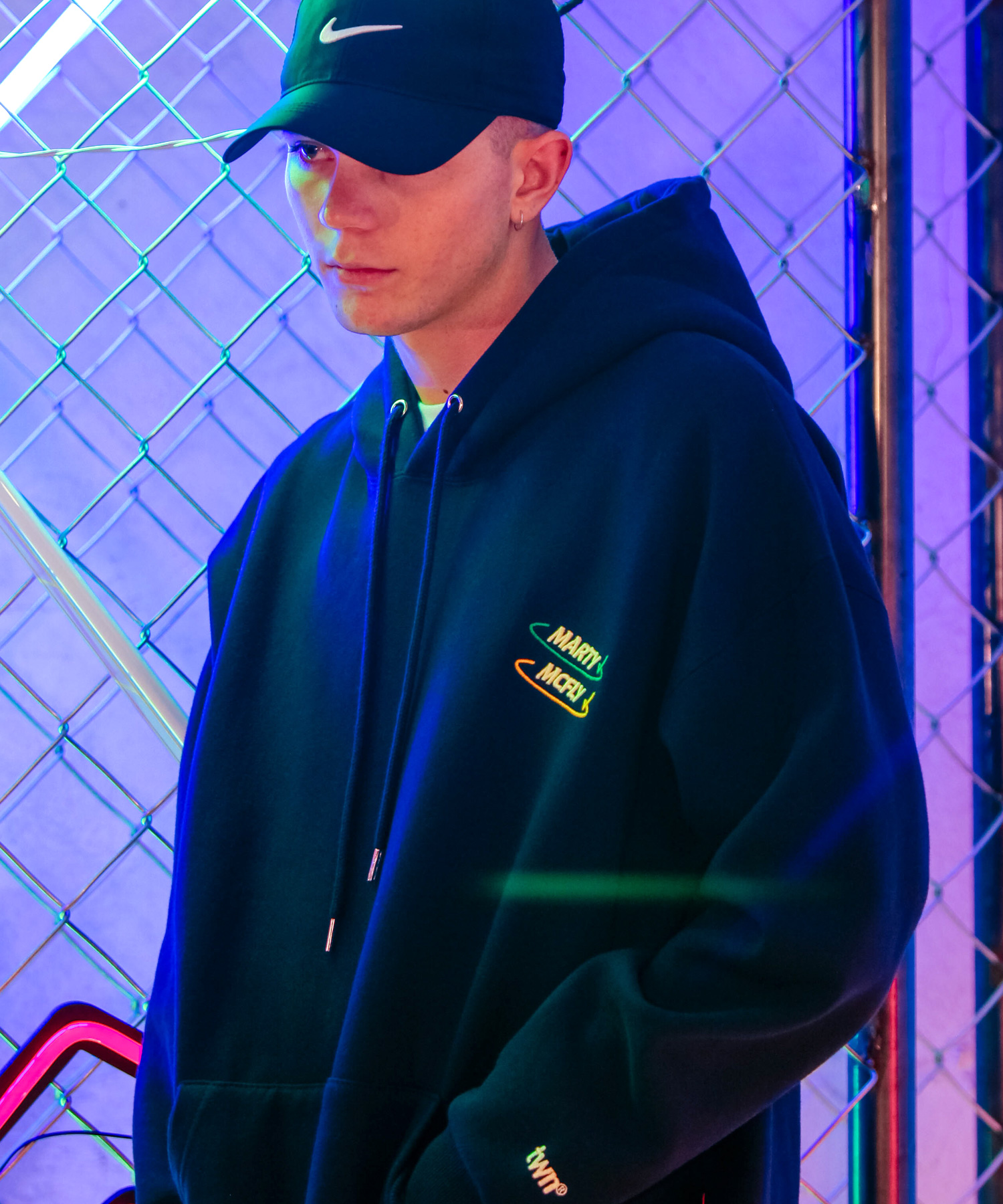 네이비 오버핏 후드티. 왼쪽 가슴에 그린·옐로 타원 궤도 두 줄로 감싼 'MARTY McFLY' 자수, 소매 끝에도 작은 로고 자수