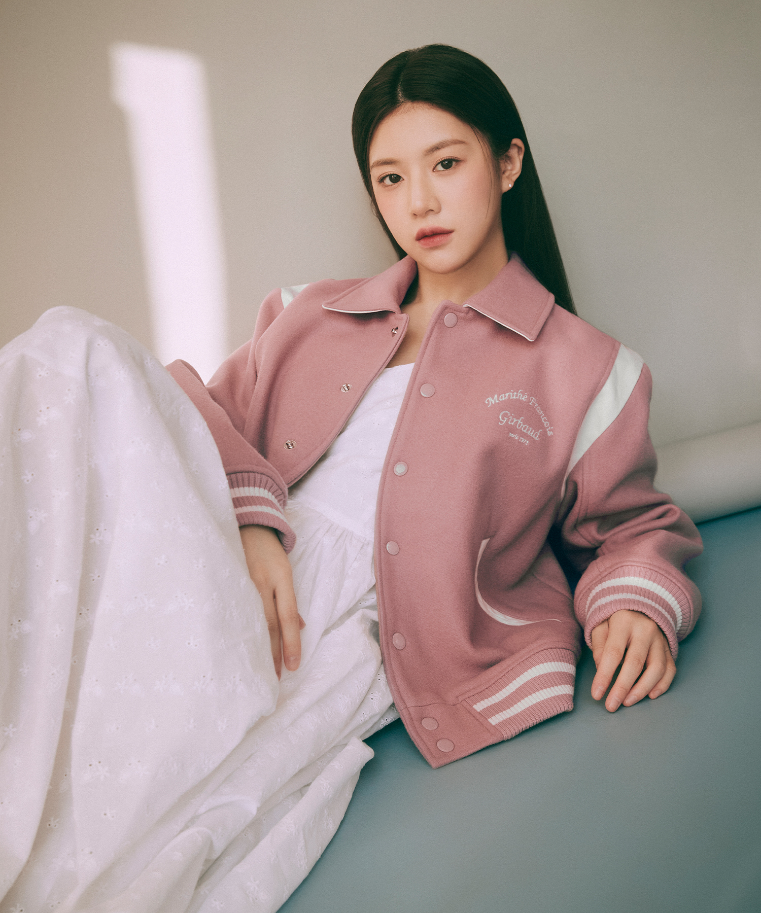 신민규와의 데이트 장면에서 입은 핑크 울 바시티 자켓. 셔츠 카라에 스냅 여밈, 왼쪽 가슴에 필기체 브랜드 로고 자수, 어깨에 화이트 배색 패널, 소매 끝 립 커프에 화이트 스트라이프 2줄