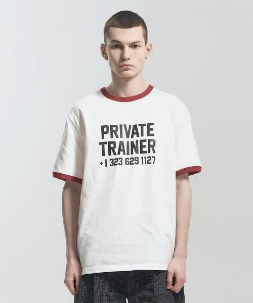 흰색 링거 티셔츠. 목과 소매 끝에 버건디 배색이 들어가고 가슴에 PRIVATE TRAINER 레터링이 크게 프린트됐다
