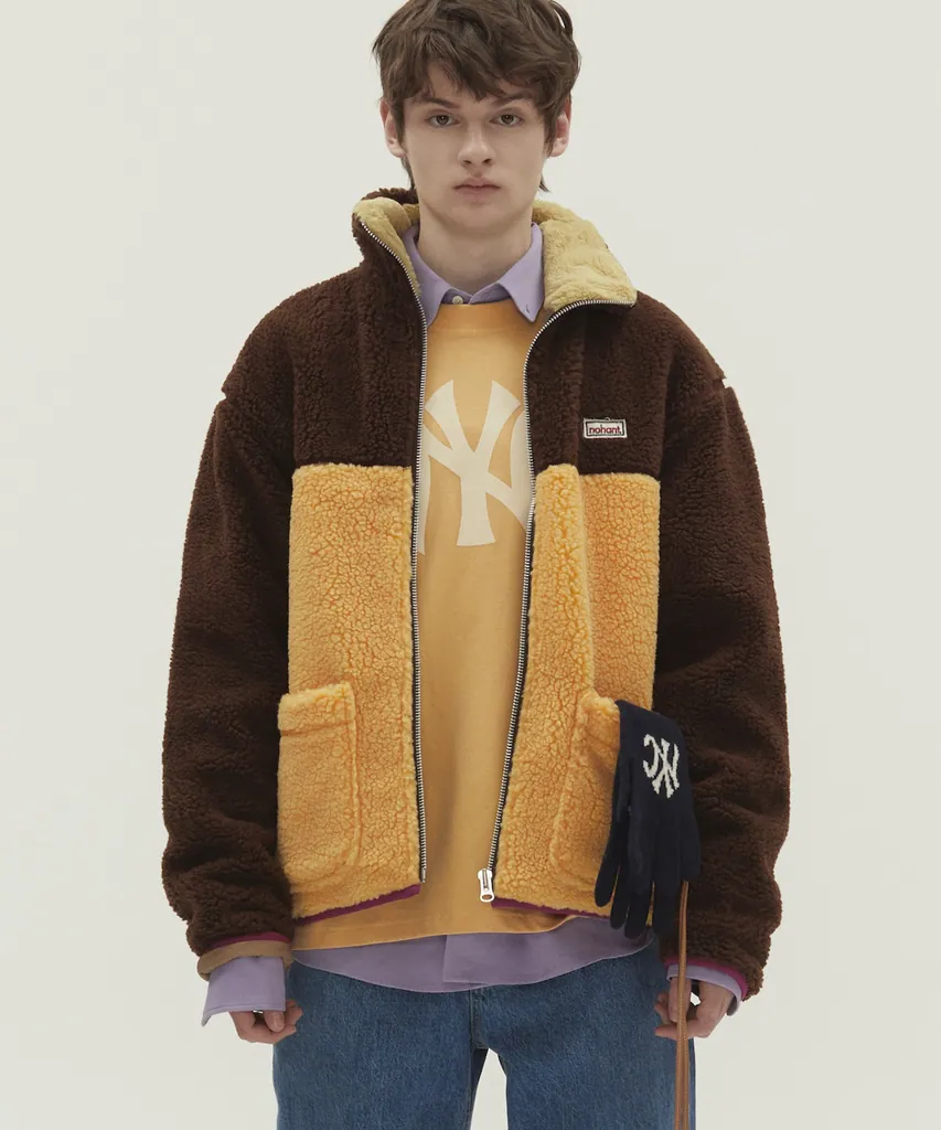 진갈색 보아 플리스 집업 점퍼. 가슴 윗부분은 진갈색, 몸판 아래는 오렌지(머스터드) 컬러블록에 양쪽 큼직한 패치 포켓, 가슴 왼쪽에 작은 로고 패치, 지퍼 안쪽 마젠타 파이핑.