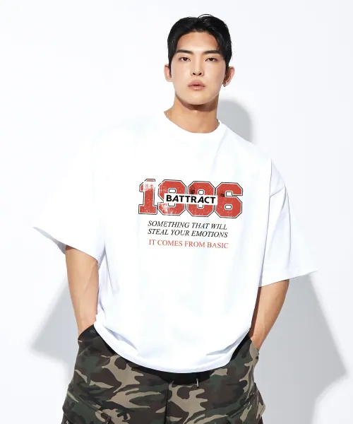 다리 아래 야외 장면에서 입은 화이트 오버핏 반팔티. 가슴 앞 레드 1986 숫자와 영문 문구 프린트