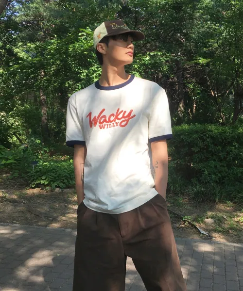 실내 장면에서 후드 집업 안에 입은 크림 링거 반팔티. 가슴 레드 필기체 로고, 블랙 라인 넥