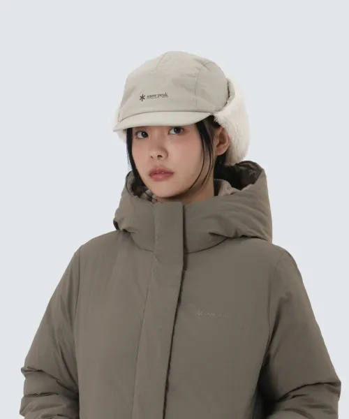 퍼 안감 이어플랩이 달린 라이트 베이지 패딩 캡. 새벽 야외 장면에서 착용했고 정면 작은 로고가 보인다.
