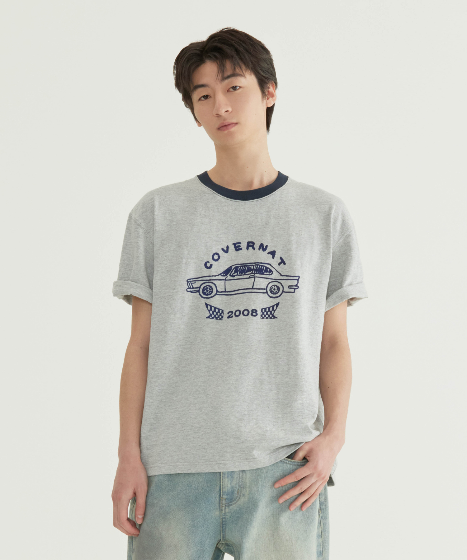 차 안 이동 장면과 계곡 야외 장면에서 입은 멜란지 그레이 슬럽 반팔 티. 네이비 링거 넥, 가슴 중앙 COVERNAT 아치 레터링 아래 빈티지 자동차 라인 드로잉과 2008 체커 플래그