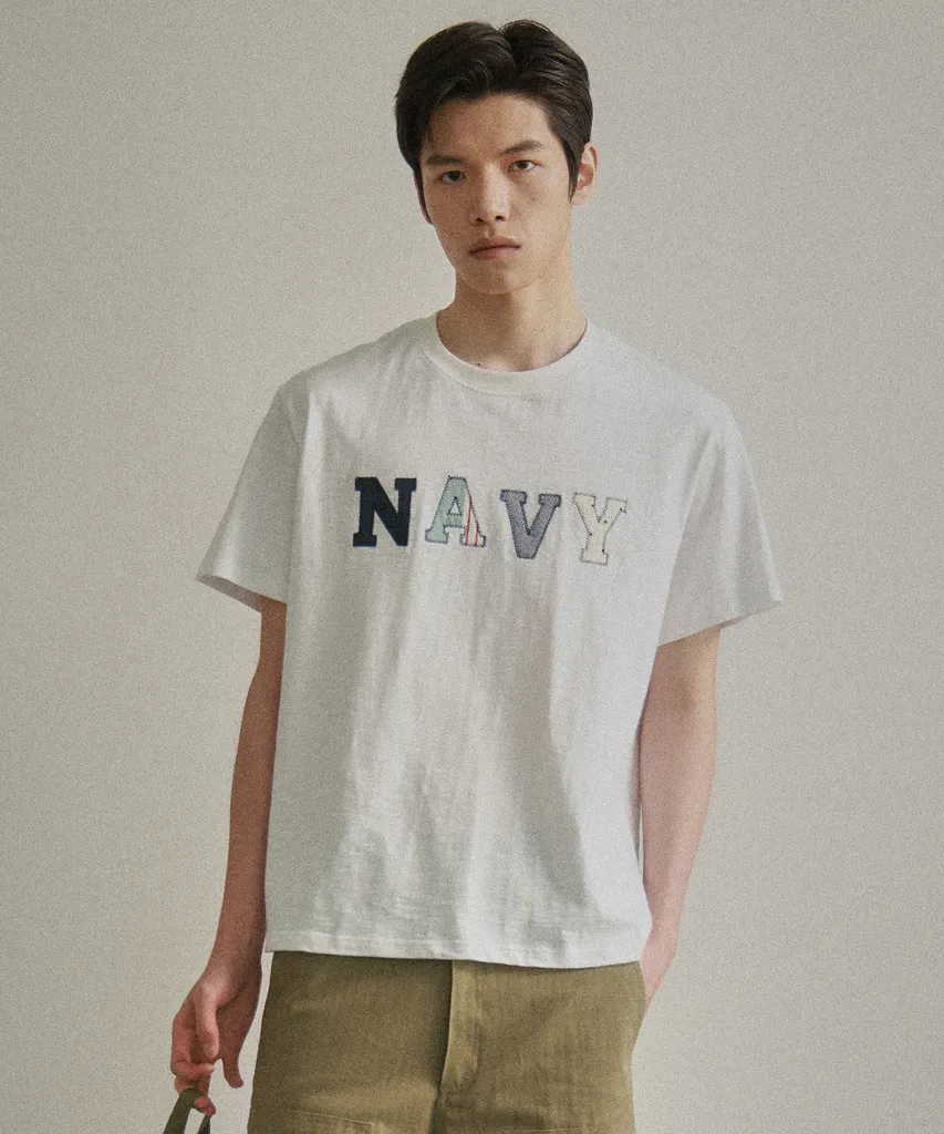 워크 재킷 안에 입은 화이트 슬럽 반팔 티. 가슴에 글자마다 다른 원단 패치워크 'NAVY' 레터링