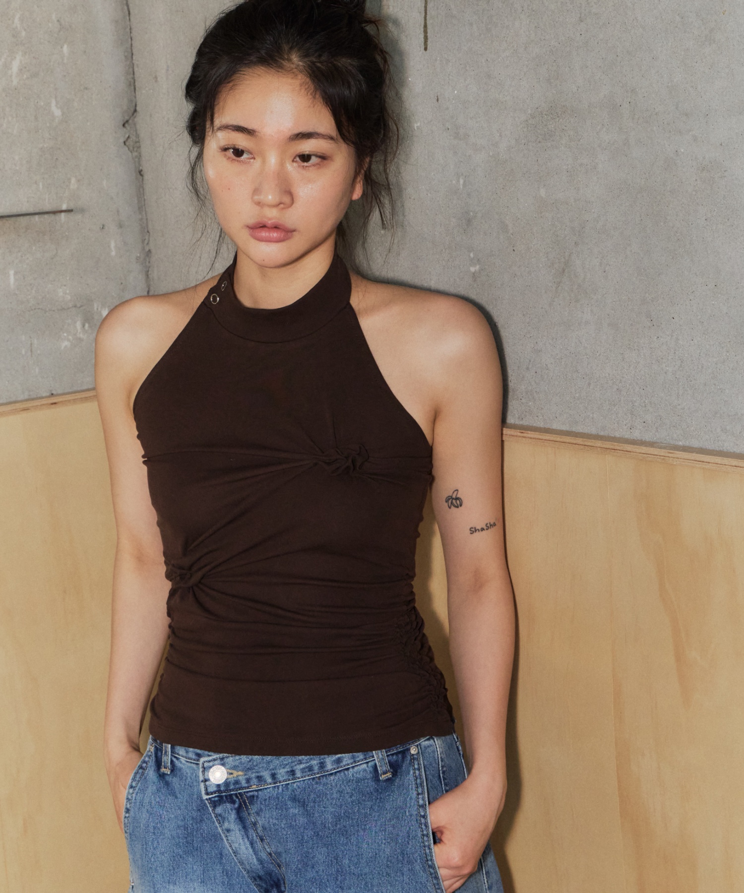 다크 브라운 하이넥 홀터 슬리브리스 톱. 넥밴드 옆쪽 스냅 여밈, 가슴 중앙과 옆 허리에 원단을 꼬아 잡은 매듭 디테일과 옆선 셔링
