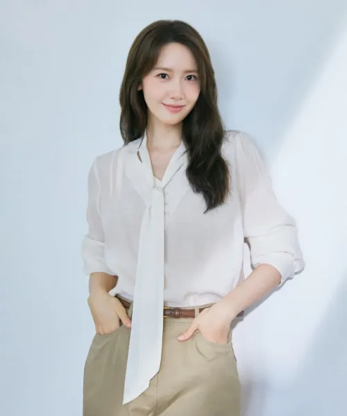 주현영이 아이보리 시어 소재 브이넥 타이 블라우스를 입고 이야기를 듣는 장면.