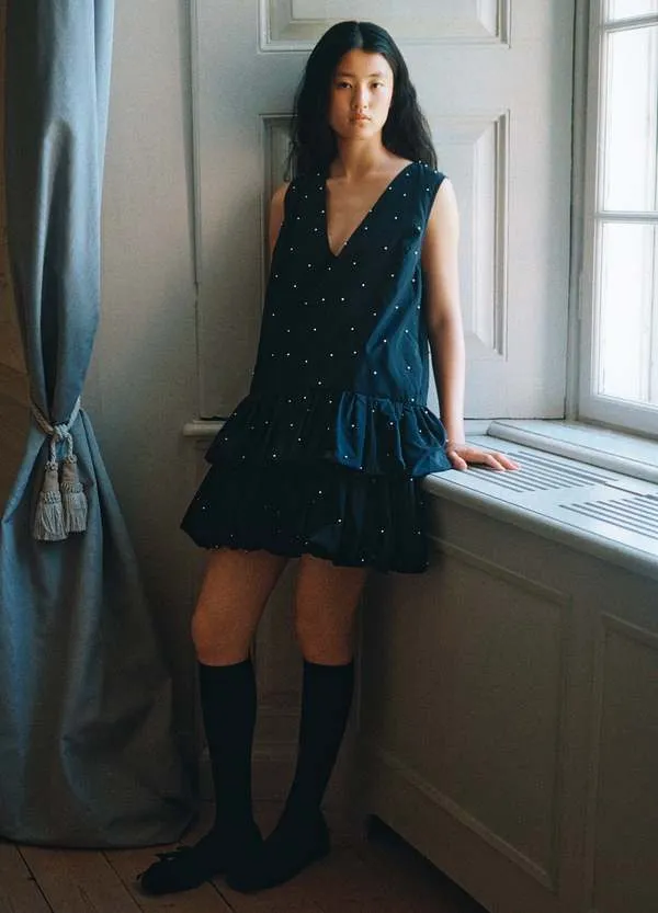 블랙 브이넥 민소매 미니 원피스, 흰 진주 비즈가 전체에 박히고 하단은 티어드 버블 헴.