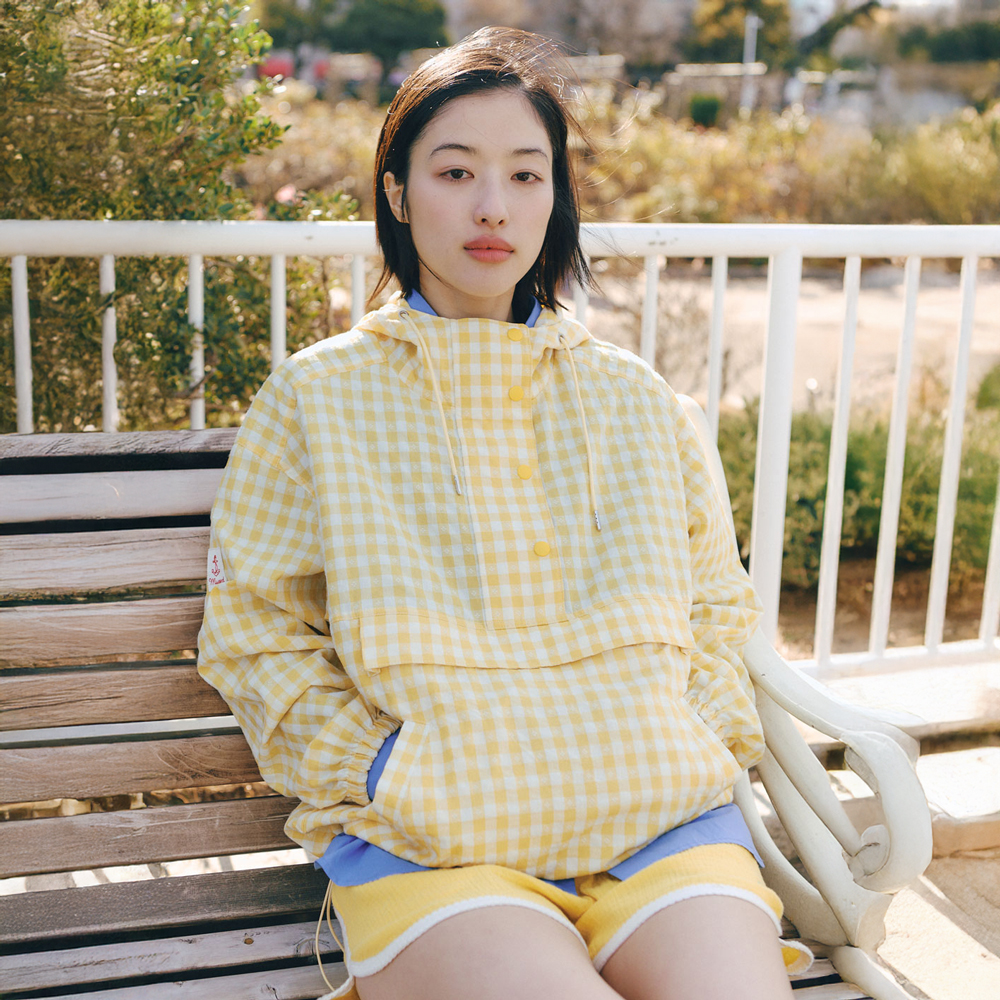 옐로·화이트 깅엄체크 오버사이즈 아노락. 배를 가로지르는 절개선 위 캥거루 포켓과 블루 안감 후드가 대비를 만든다