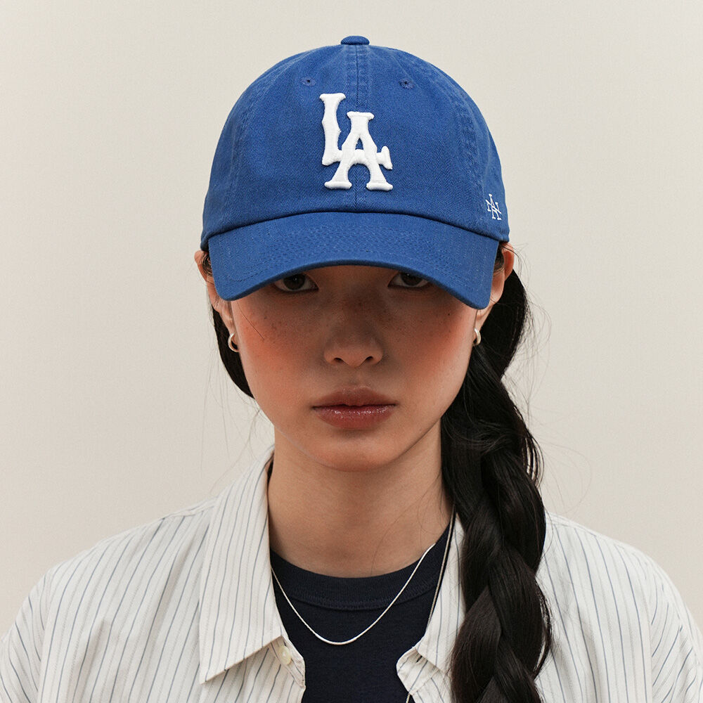 행사장 게임 구간에서 라이트블루 셔츠와 함께 쓴 볼캡. 로얄 블루 코튼 6패널에 앞면 화이트 입체 LA 자수, 측면에 작은 브랜드 모노그램 자수, 심지 없는 언스트럭처 크라운과 곡선 챙