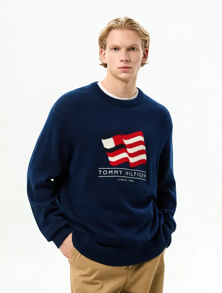 네이비 니트 가슴 중앙에 레드·화이트 물결 플래그와 TOMMY HILFIGER SINCE 1985 문구가 들어간 리브 넥 크루넥 스웨터.
