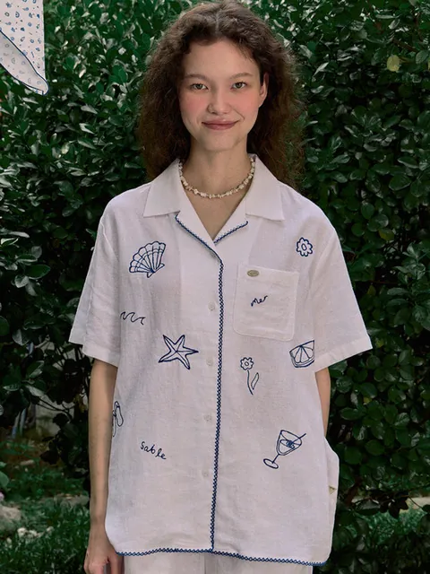 화이트 오픈칼라 반소매 셔츠. 조개·불가사리·칵테일 등을 그린 블루 선화 자수와 블루 트림이 들어간다