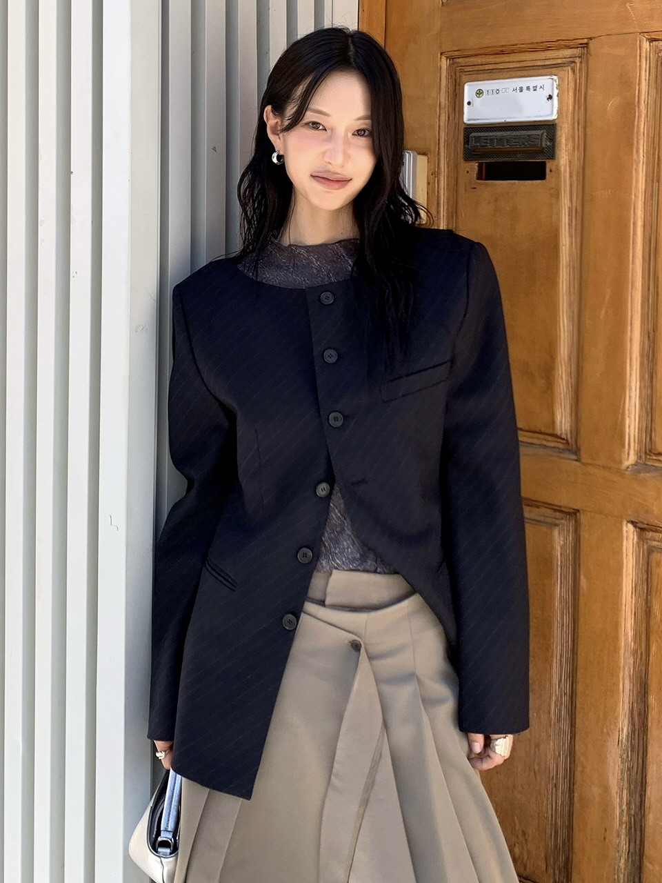 칼라 없이 넓게 파인 보트넥 네이비 자켓. 같은 색 실로 넣은 사선 스트라이프가 톤온톤으로 비치고 앞단은 단추 하나씩 세로로 이어진다