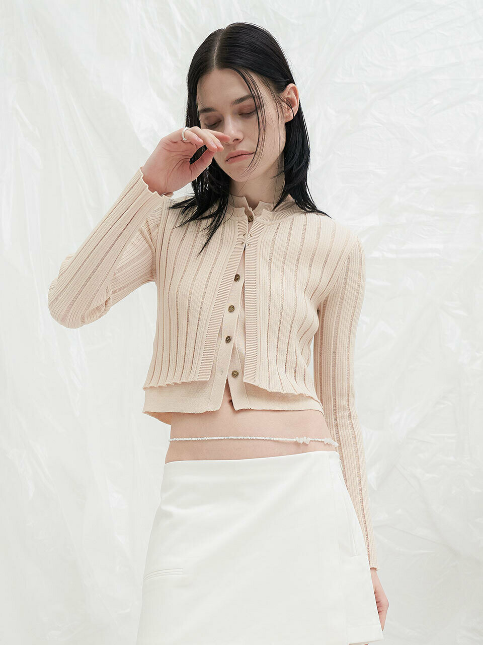 가디건 두 장을 겹쳐 입은 것처럼 보이는 크림 골지 가디건. 안쪽 레이어가 밑단 아래로 살짝 내려오고, 앞판 골드 톤 작은 단추 6개 여밈에 짧은 기장