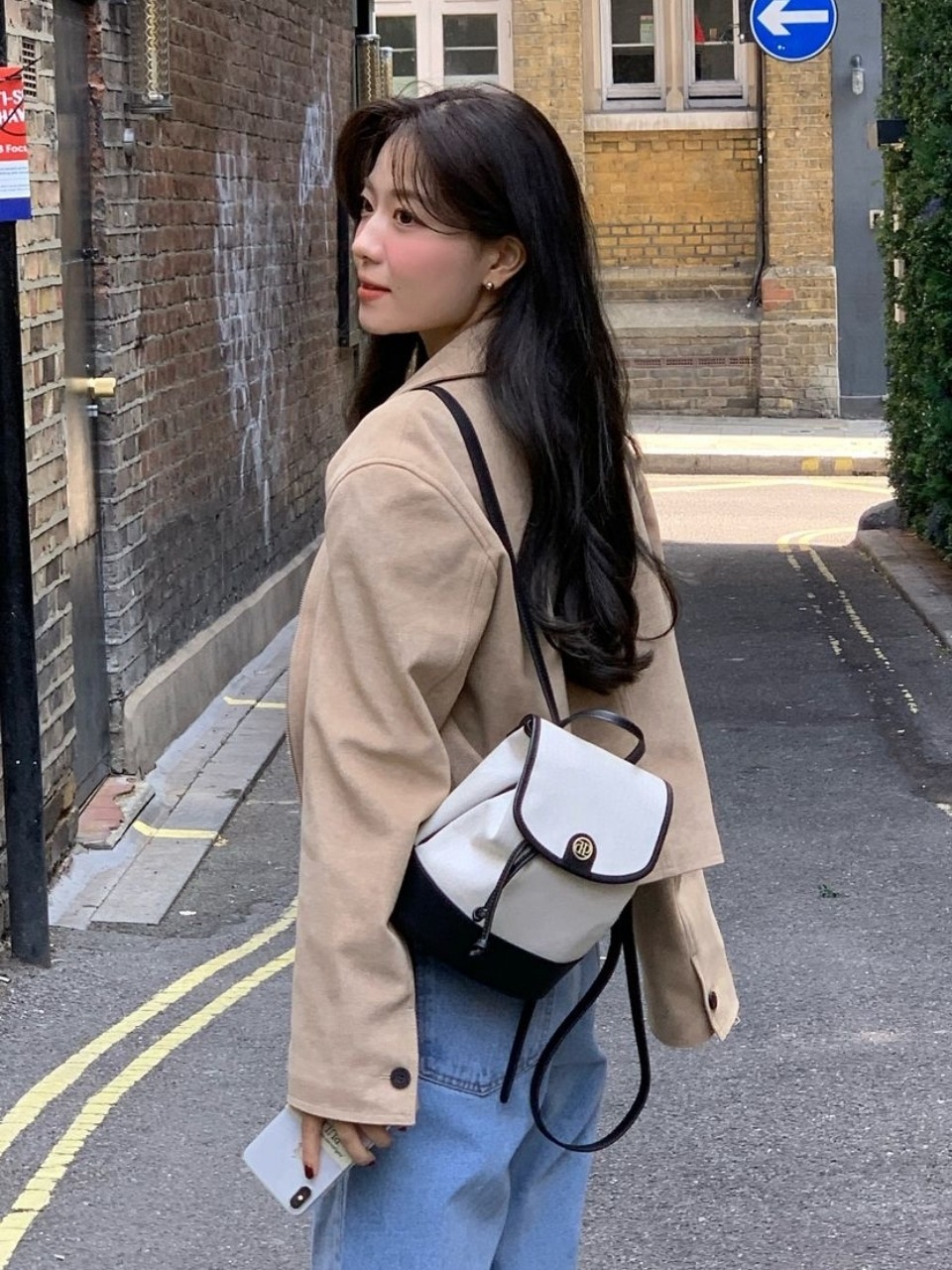 퇴근 장면에 멘 작은 미니 백팩. 아이보리 헤링본 패브릭 바디에 블랙 가죽 파이핑·스트랩, 플랩 중앙 골드 로고 장식, 조임끈이 달린 입구